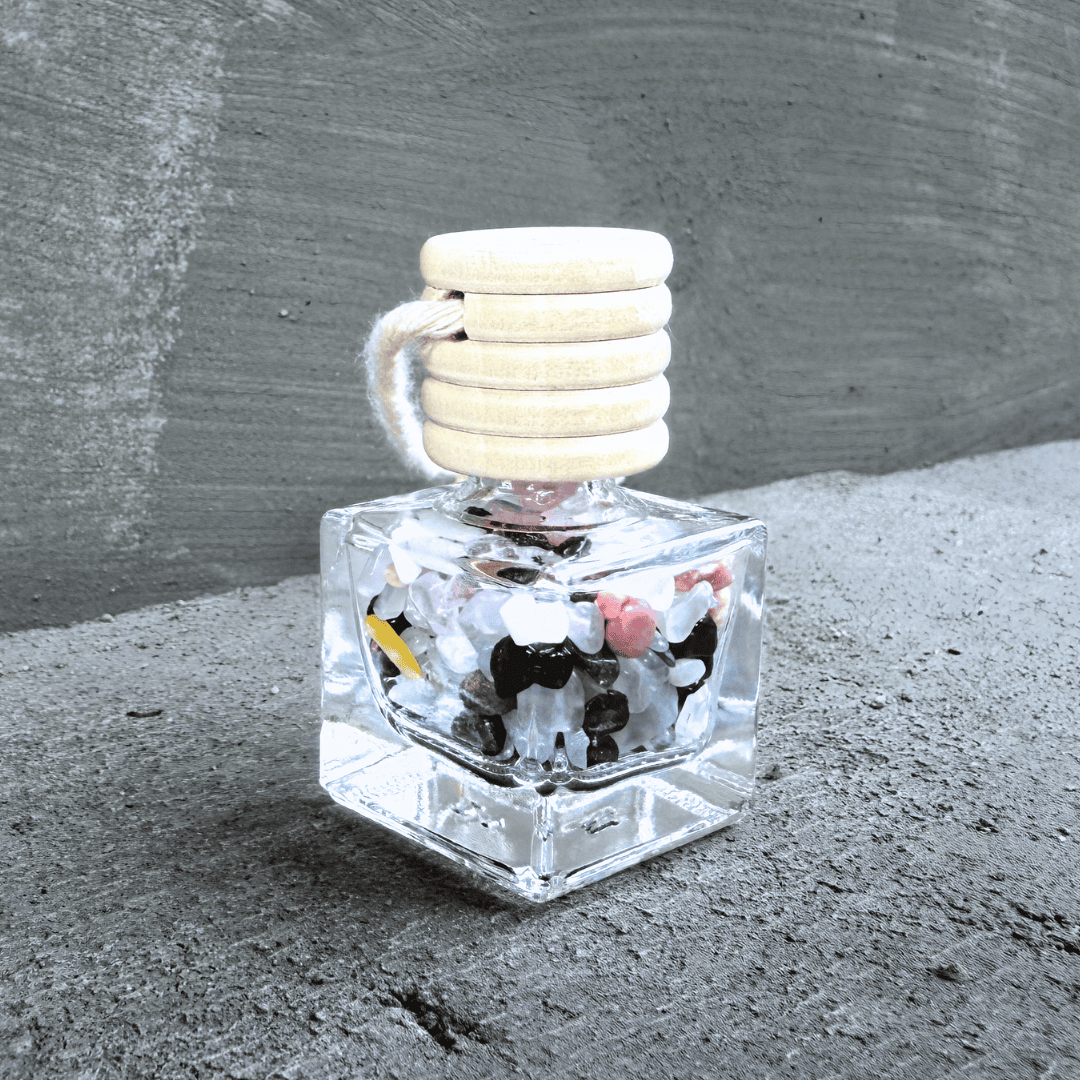 Detailní pohled na talisman Hecatoo Láska z minerálů granát, růženín, ametyst, měsíční kámen a rodonit ve skleněné lahvičce s provázkem.